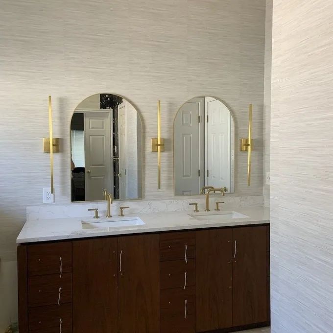 A stylish bathroom vanity featuring double sinks, elegant wall-mounted faucets, and two mirrors flanked by sophisticated sconce lighting.