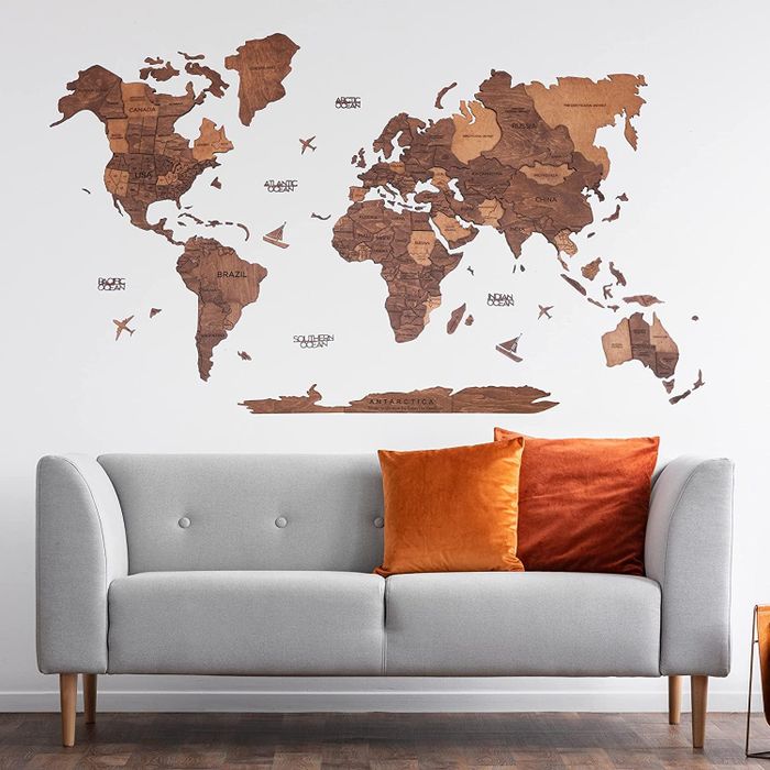Wooden world map wall art positioned above a contemporary gray sofa with vibrant orange throw pillows.