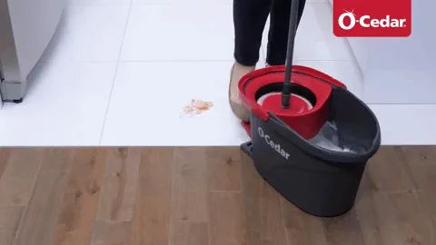 A person using the foot pedal on a water basin to wring out a small mop.