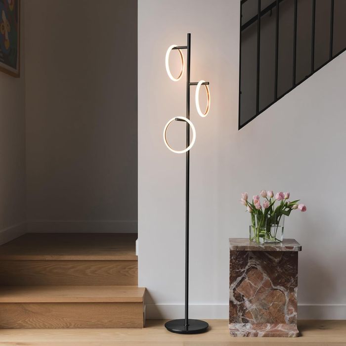 A contemporary floor lamp featuring circular lights beside a marble table adorned with pink tulips, set in a chic home interior