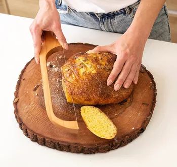 A person slicing bread on a wooden cutting board with a bread knife.