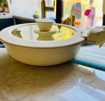 A kitchen countertop displaying a ceramic skillet with a glass lid, surrounded by dish soap and other cleaning supplies.