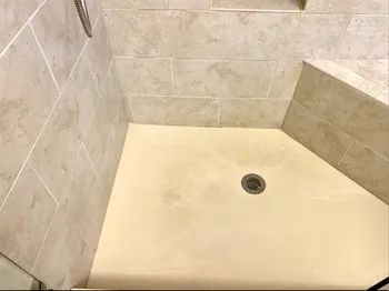 A dirty shower with a yellowing floor.