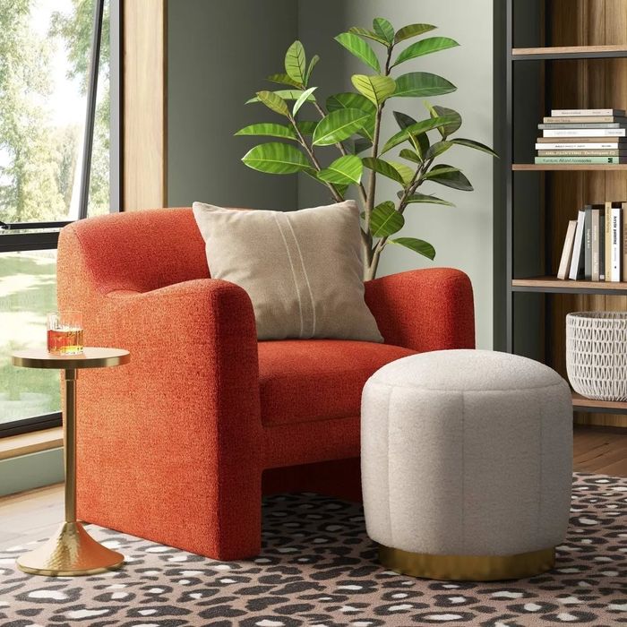 The tufted faux shearling ottoman with a brass base, set against a cozy living room backdrop