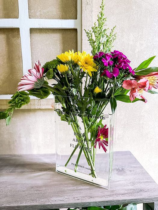 A clear book-style vase beautifully arranged with a lush bouquet, making a striking statement in any room.