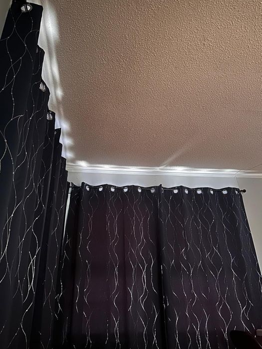 Thick dark curtains with a wavy pattern, hanging from a ceiling, blocking light and creating a cozy vibe
