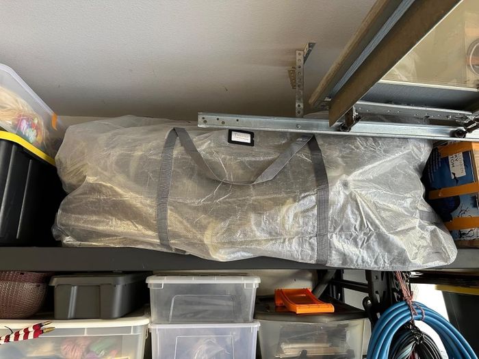 A spacious bag placed on a garage shelf, surrounded by clear plastic bins and neatly coiled cables
