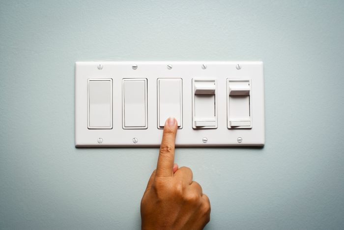 A hand flipping one switch among a group of five on a wall