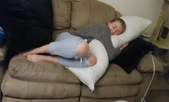 A person lounging on a couch, hugging a large pillow, dressed in a sweater and ripped jeans. A cozy, relaxed atmosphere