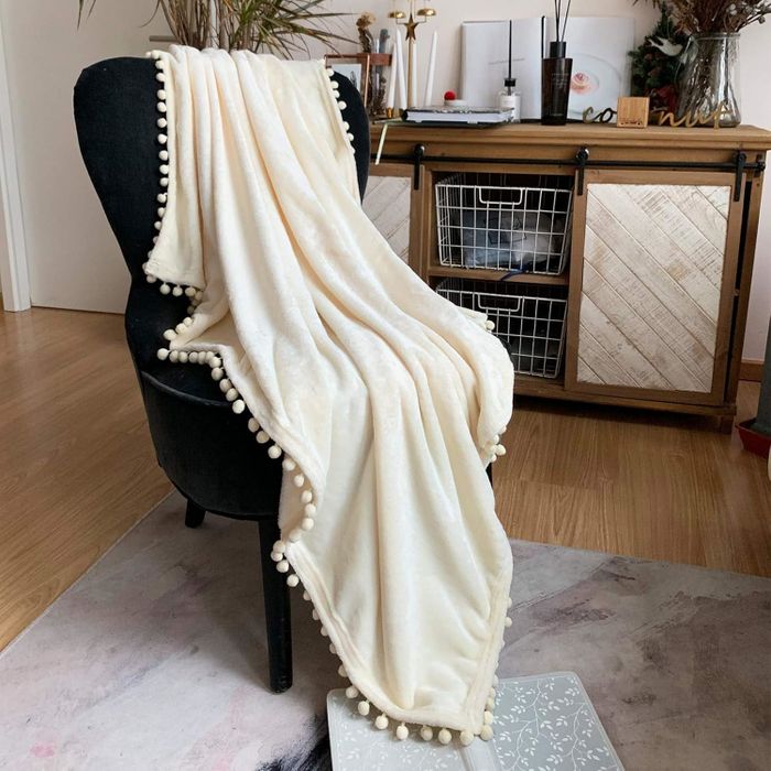 An ivory blanket with pom-pom trim elegantly thrown over a black chair.