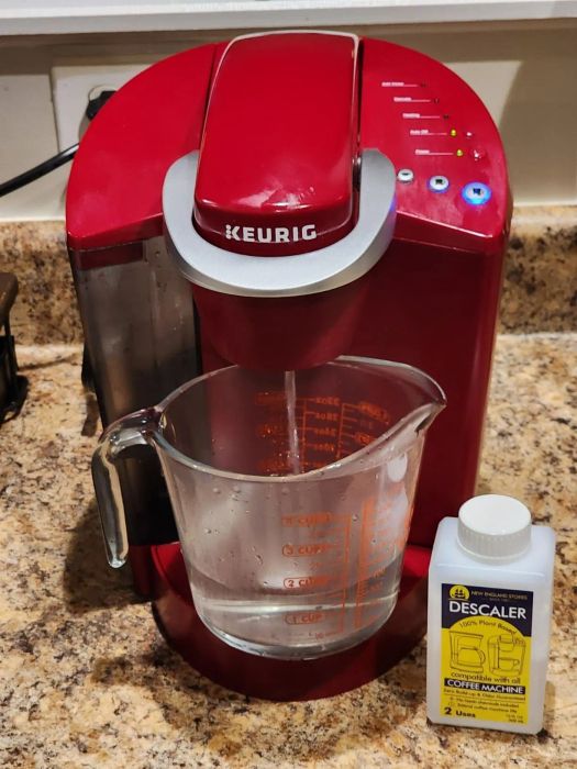 A Keurig coffee maker on a kitchen counter, accompanied by a measuring cup and a bottle of descaler.