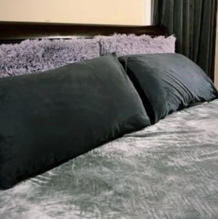 A neatly made bed with rich dark bedding and a collection of fluffy pillows, placed against a light-colored wall and dark curtains