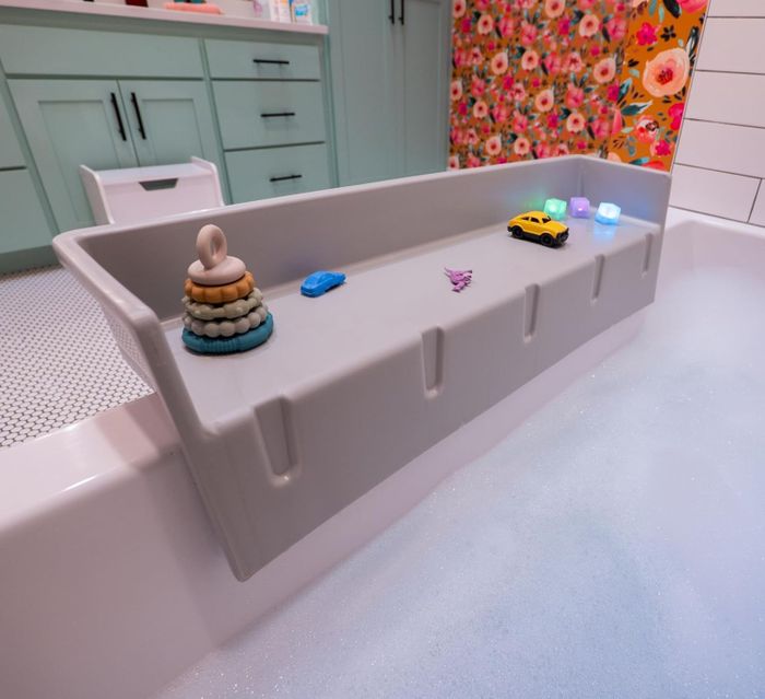 The gray bathtub topper attached to the lip of the tub with toys on it, providing a play area.