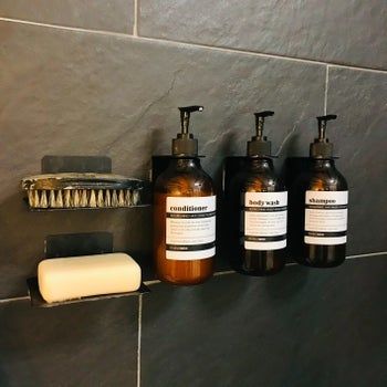 A reviewer's neatly organized shampoo, conditioner, and body wash bottles displayed on the wall of their shower.