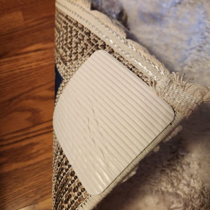A rug corner lifted, showing a non-slip grip pad underneath on a hardwood floor. Ideal for improving home safety and convenience.