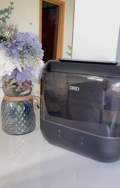 A stylish Dreo air fryer placed on a kitchen counter beside a decorative vase filled with fresh flowers.