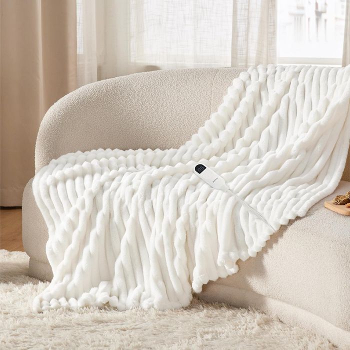 A plush white throw blanket with a ribbed texture, casually draped over a couch, next to a remote control, set in a warm and inviting living room