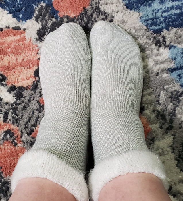 Two feet, wrapped in cozy, light-colored socks, rest comfortably on a patterned rug, perfect for an article on home comfort apparel.