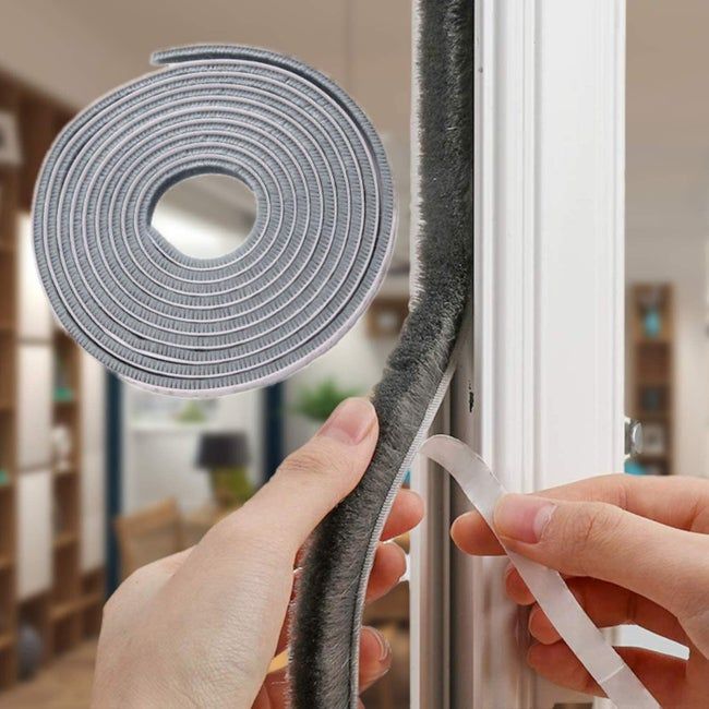Someone applying weatherstripping to a window, peeling off the adhesive tape from the back of the roll