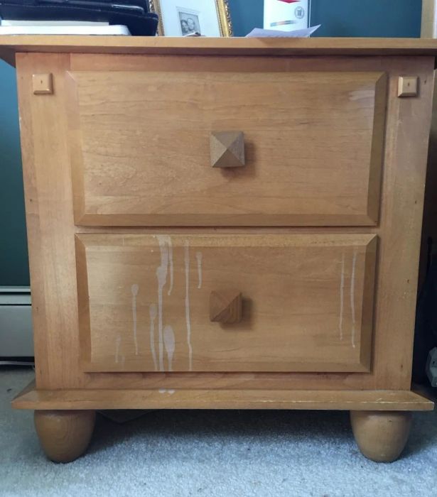 A reviewer's photo of a light wood nightstand with visible white water stains dripped down the front.