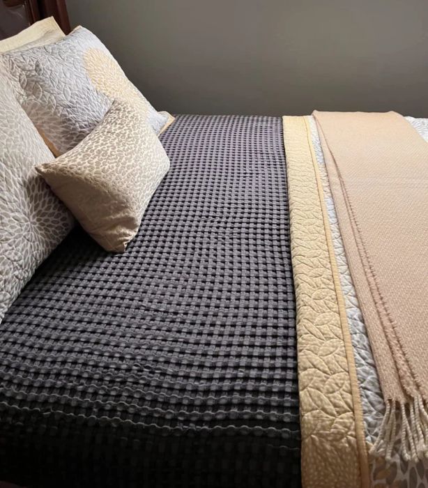A carefully made bed with a textured comforter, a decorative pillow, and neatly folded blankets on the side
