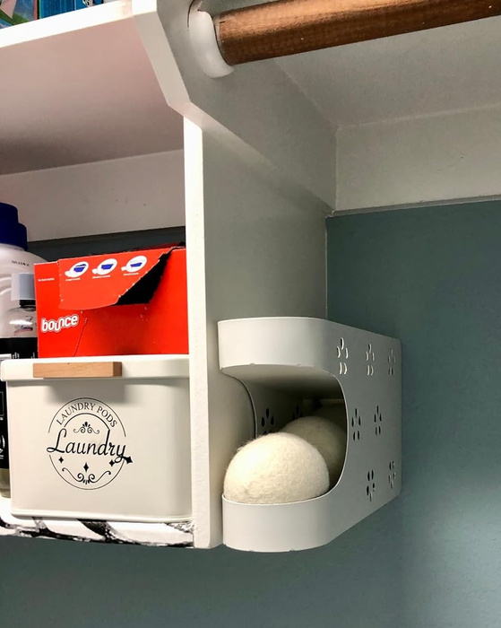 A wall-mounted laundry dispenser with wool dryer balls and a box of fabric softener sheets placed on a shelf above.