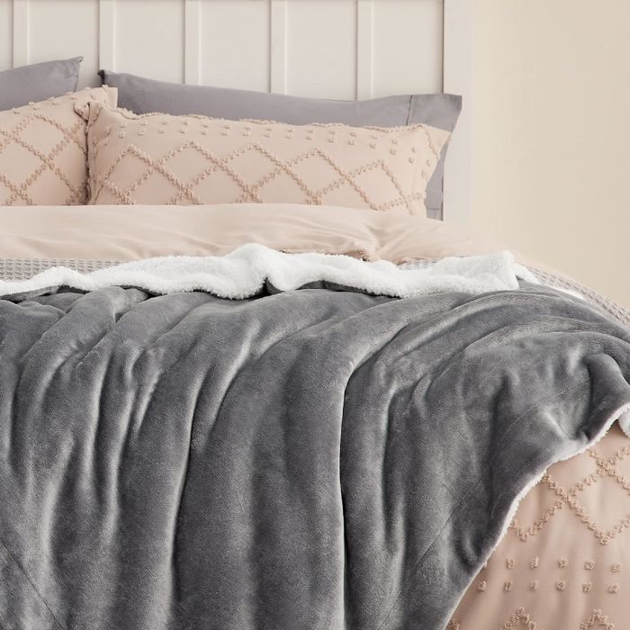 A plush gray blanket draped over a neatly made bed, with decorative pillows adding a touch of style