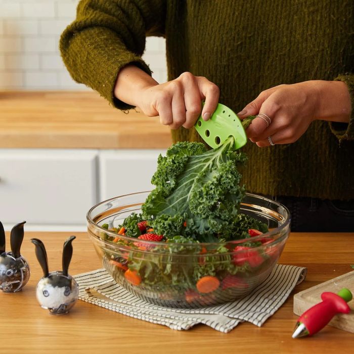 Someone using a kale stripper to remove leaves from the stems and drop them into a salad bowl in a kitchen.