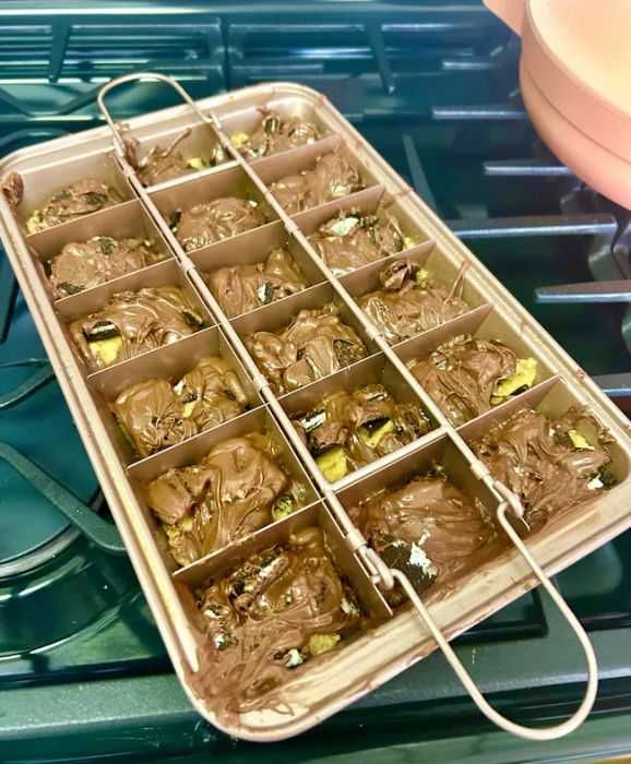 A copper-colored brownie pan with 18 evenly divided slots and a removable divider on top, holding freshly baked brownies.