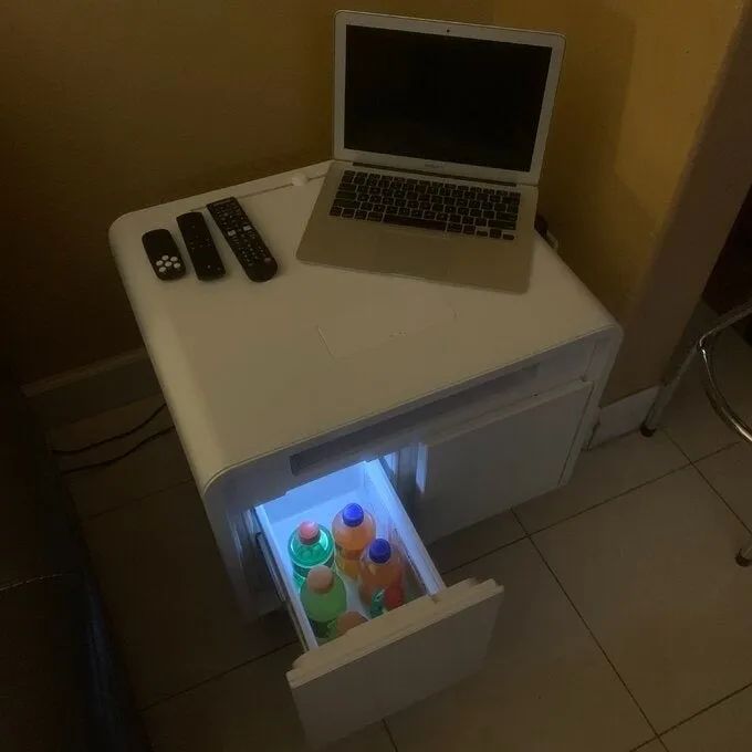 a reviewer photo showing the white nightstand with an open drawer holding drinks, next to a laptop and remote controls