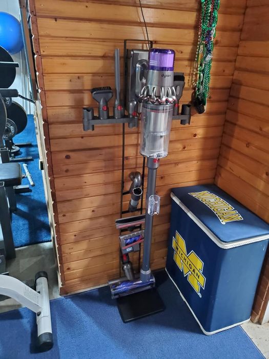 A Dyson vacuum mounted on a charging dock in a home gym setup, placed next to a cooler.