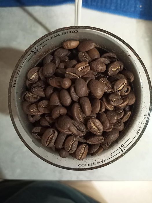 A close-up of coffee beans in a white measuring cup, with various units marked on the side, viewed from above.