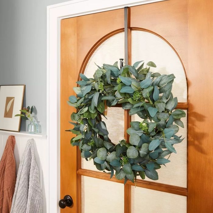 A wreath adorned with green leaves and delicate flowers hanging on a wooden door