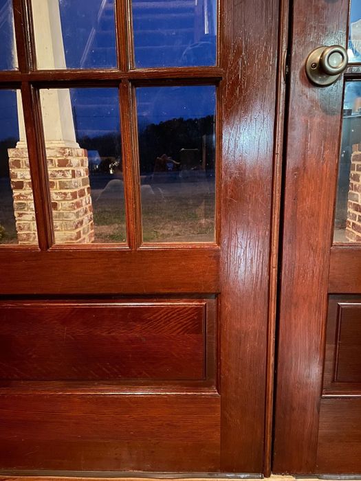 A view through a windowed wooden door, capturing an outdoor patio scene at dusk, with a brick column and suburban landscape in the background.