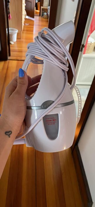 A hand gripping a Conair steamer with its coiled cord, ready for action indoors.