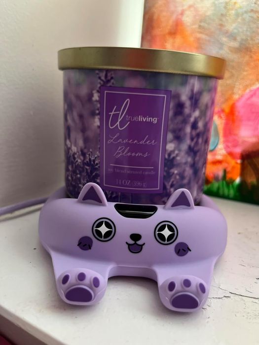 A lavender-scented candle resting on a purple cat-shaped warmer