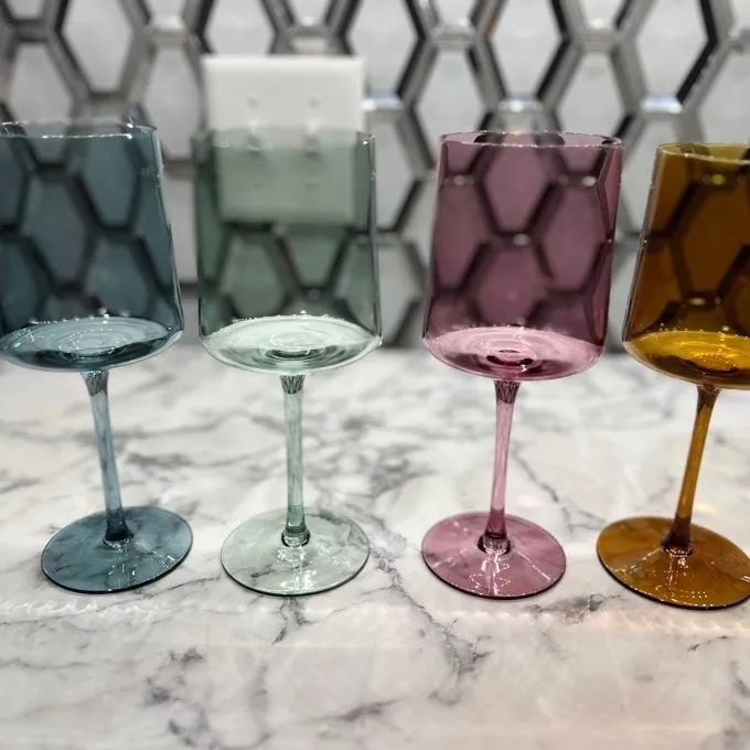 Four elegantly designed, multicolored wine glasses displayed on a sleek marble surface, with a chic geometric tile backsplash enhancing the background.