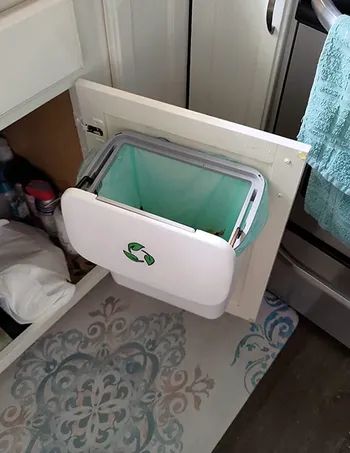 The white version of the compost bin with the lid slid open, revealing the top of the can.