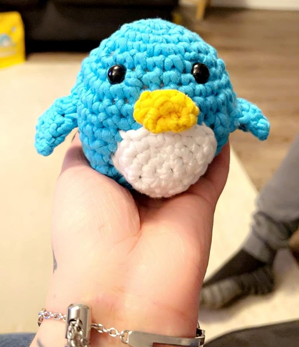 A hand holding a crocheted penguin, showcasing the finished project.