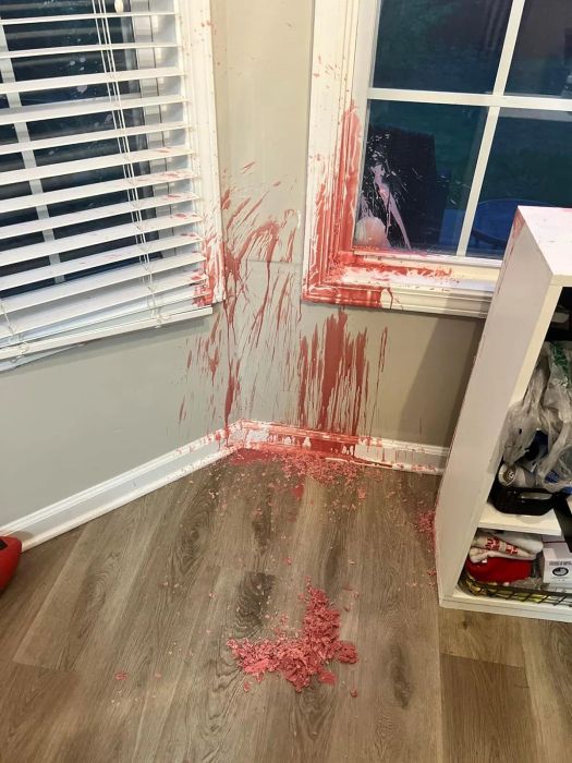 Spilled pink wax splattered on the corner of a room, covering the floor and window ledge, with some of the substance pooled on the floor.