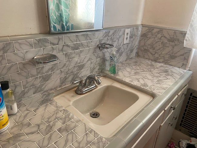 A reviewer's bathroom vanity and sink showcasing the peel-and-stick faux-marble tiles.