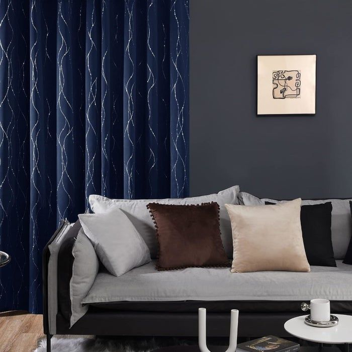 A modern living room featuring a gray sofa with colorful pillows, dark curtains, and abstract art, creating a warm and inviting atmosphere