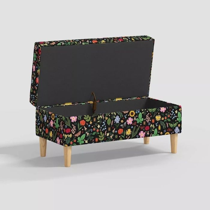 A rectangular storage bench with an open lid, showcasing vibrant multicolored floral patterns and supported by wooden legs