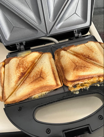 Two grilled sandwiches filled with melted cheese, cooking in a sandwich maker