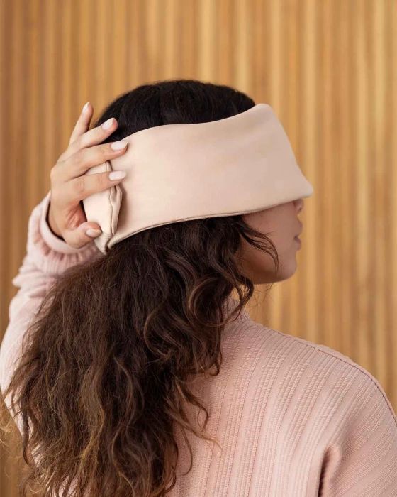 A person wearing a soft pink headband over their eyes, ensuring a peaceful rest