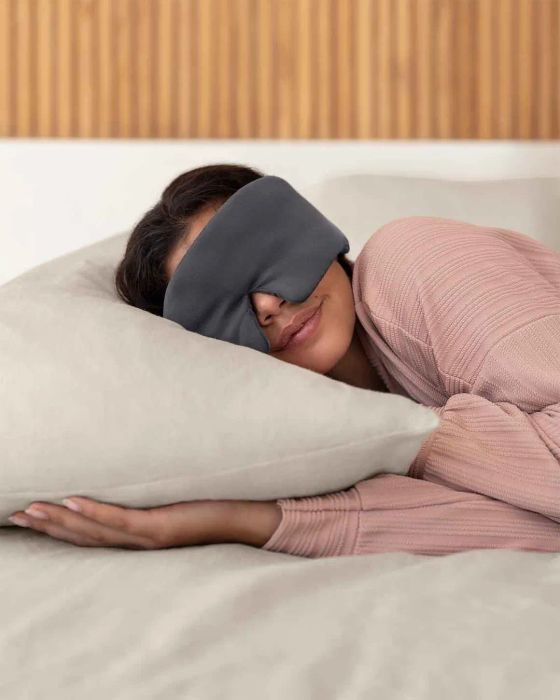 A person relaxing with a sleep mask, comfortably resting on a pillow in cozy sleepwear