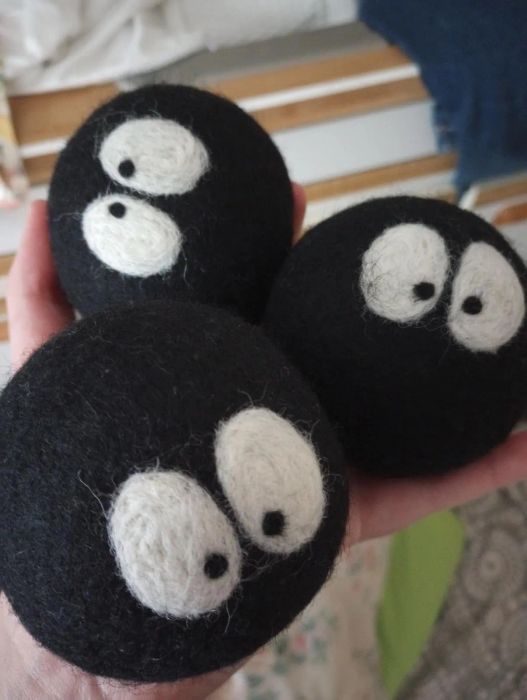 Hand holding three black wool dryer balls with cute white animated eyes. Perfect for laundry and eco-friendly shopping choices