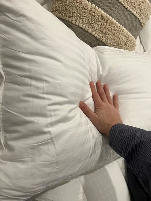 A person pressing down on a white striped pillow to demonstrate its softness and fluffiness