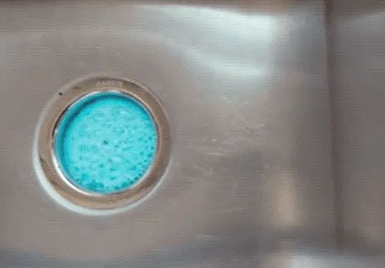 Blue foaming cleanser making its way out of the sink drain.
