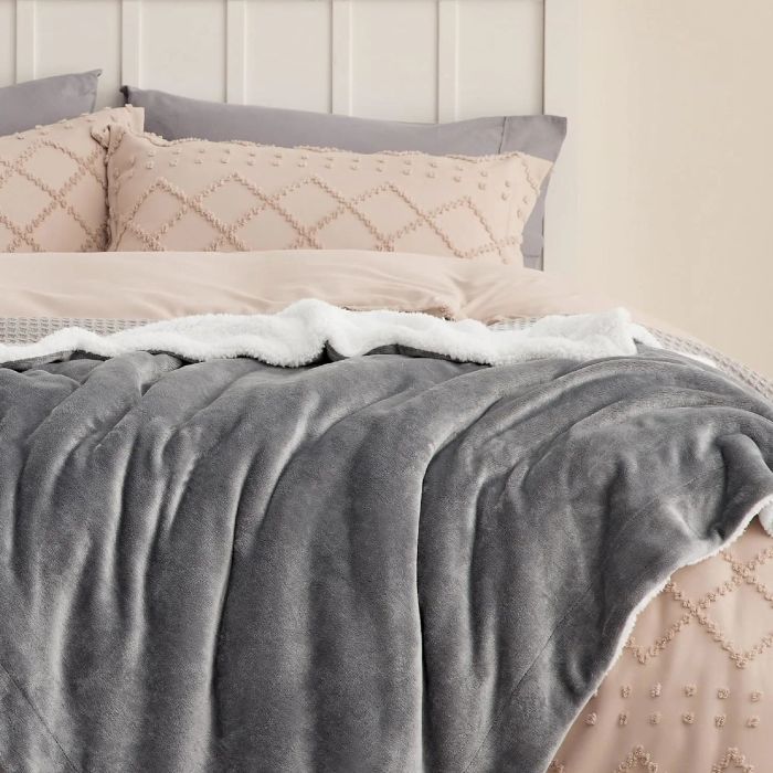A plush gray blanket spread across a neatly made bed, complemented by decorative pillows